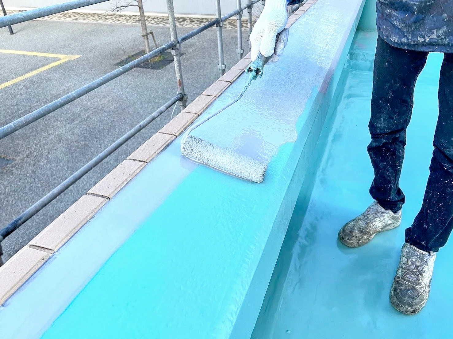 防水塗装工事の施工風景。青い防水塗料をローラーで建物表面に塗布している作業員の様子。